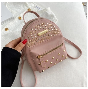 Pink mini leather backpack with gold studs and front pocket held by model in hand