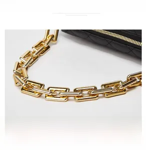 Macro shot of high-shine gold rectangular chain handle on black quilted handbag