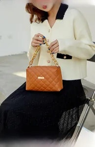 Detail of a brown quilted handbag with chunky gold chain strap worn by a model
