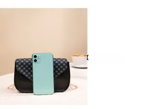 Size comparison of black printed saddle bag with gold chain next to a smartphone