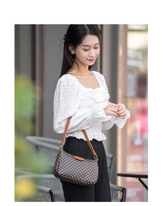 Close-up of printed shoulder bag with brown leather strap worn with white ruffle blouse