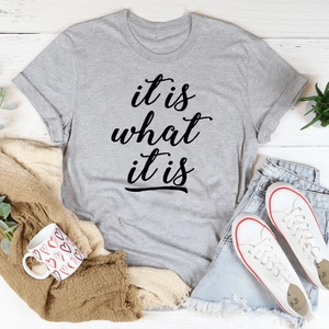 Flachbild eines grauen Baumwoll-T-Shirts mit Aufdruck it is what it is auf Holzhintergrund