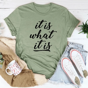 Flatlay des grünen 'it is what it is' Baumwoll-T-Shirts mit Jeans-Shorts und Deko