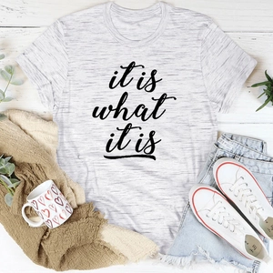 Graues T-Shirt mit it is what it is Aufdruck auf weißem Holzgrund im Flatlay-Stil