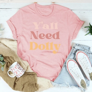 T-shirt rose Y'all Need Dolly posé avec jean et accessoires sur fond de bois