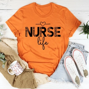 Flat lay of an orange NURSE Life t-shirt with leopard print text on white wood background