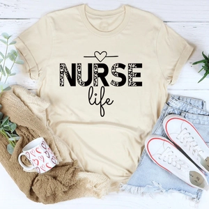 Flat lay of a beige NURSE life T-shirt with leopard print text and casual accessories