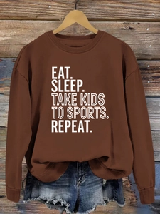 Détail du sweat marron avec slogan Eat Sleep Take Kids To Sports sur fond bois