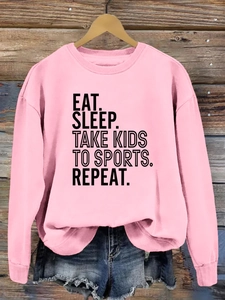 Détail d'un sweat rose avec imprimé 'EAT SLEEP TAKE KIDS' sur un fond en bois rustique