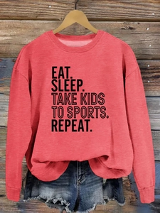 Gros plan du slogan EAT SLEEP TAKE KIDS TO SPORTS imprimé sur un sweat-shirt corail rouge
