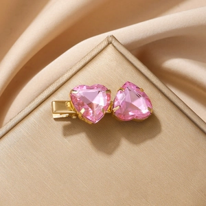 Elegante clip de pelo dorado con dos piedras de corazón rosa sobre satén de champán