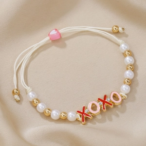 Braided XOXO bracelet with white pearls and pink heart slide on beige satin background