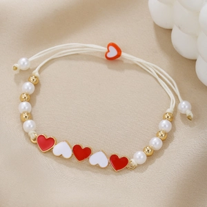 Detail of woven bracelet with red and white enamel hearts and pearls on textured fabric