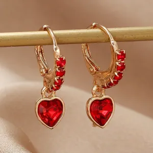 Boucles d'oreilles créoles cœur doré avec cristaux rouges sur fond de soie champagne