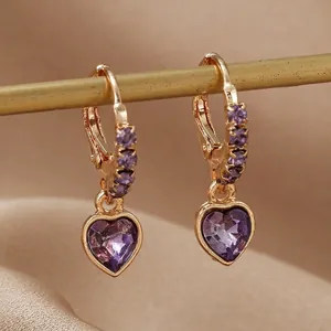 Détail de boucles d'oreilles cœur violet avec monture dorée et zircons scintillants