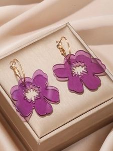 Macro shot of transparent purple acrylic flower earrings with gold metal hoops in a gift box