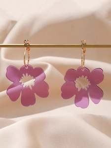 Detail of purple acrylic flower earrings hanging on a gold metal rod with silk background