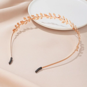 Elegant gold metal leaf headband on ceramic plate with soft champagne fabric background
