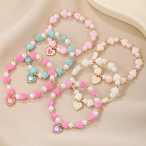 Set of five colorful beaded bracelets with heart pendants on soft textured fabric