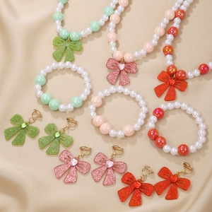 Detailed view of children's pearly bead jewelry sets with glittery bow charms on satin
