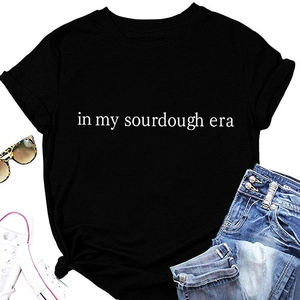 Flat lay of black T-shirt with 'in my sourdough era' print and stylish accessories