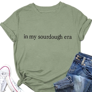 Flat lay of green cotton T-shirt featuring In My Sourdough Era text and blue jeans