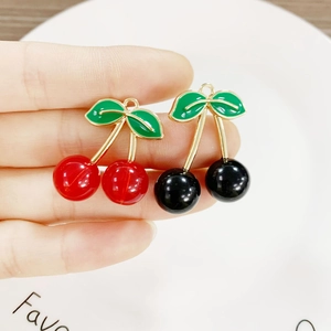 Detail of red and black cherry charms with gold branches and green enamel leaves