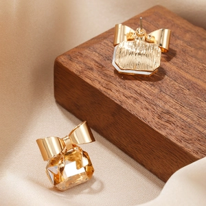 Close-up of golden bow earrings with amber square crystal on wooden display