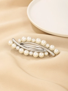Detail of silver alloy hair clip with elegant leaf design and white pearls on satin fabric