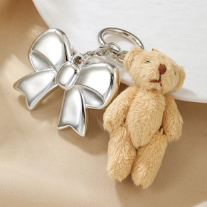 Close-up of a plush bear and polished silver bow pendant on a metal keychain