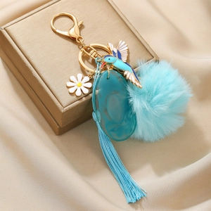 Detail of keychain featuring blue hummingbird enamel, white daisy and silk tassel accents