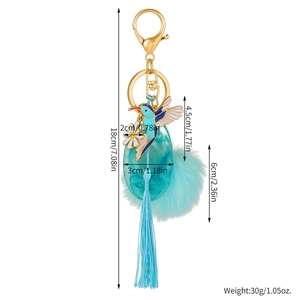 Detail of hummingbird tassel keychain with enamel bird, white daisy and blue faux fur pompom