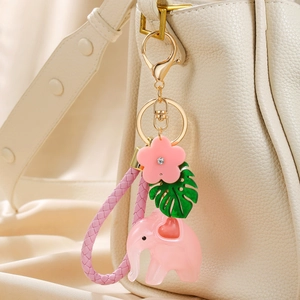 Pink elephant keychain with resin charms, monstera leaf, and braided leather strap on bag