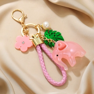 Close-up of pink acrylic elephant keychain with woven strap and floral charm on satin