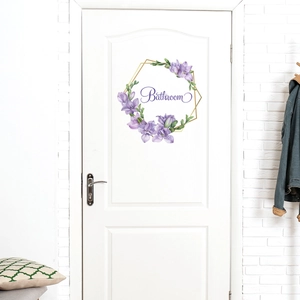 Close-up of bathroom door sticker featuring purple floral wreath and golden hexagon frame