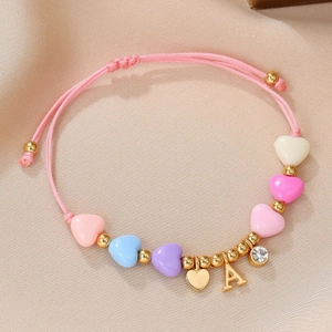 Close-up of pink handmade woven bracelet with colorful heart beads and gold letter A charm