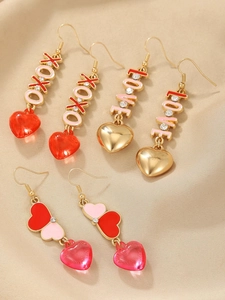 Detailed set of three heart earrings with XOXO and LOVE charms on champagne silk background