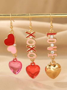 Detail of XOXO LOVE gold earrings with pink and red heart pendants on silk fabric