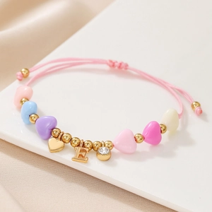 Detail of pink woven bracelet featuring macaron heart beads and gold letter E pendant