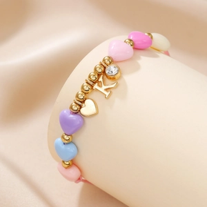 Detail of macaron heart beads with gold K letter and rhinestone charms on pink cord
