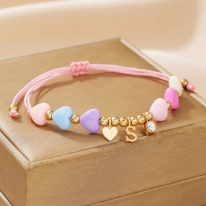 Macro detail of handmade pink braided rope bracelet with golden heart and S letter charm