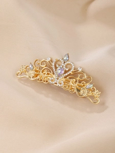 Detailed close-up of golden crown hair clip with white crystals on champagne silk background