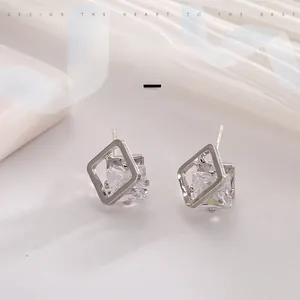 Macro shot of silver square stud earrings with clear zircon stones on silk