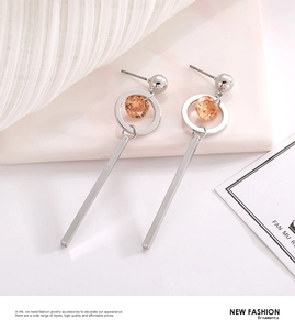 Macro detail of silver drop earrings with faceted amber crystal and geometric bar pendant