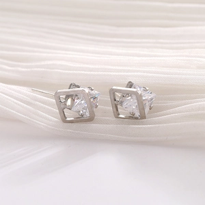 Macro shot of silver rhombic stud earrings with cubic zirconia on white pleated fabric