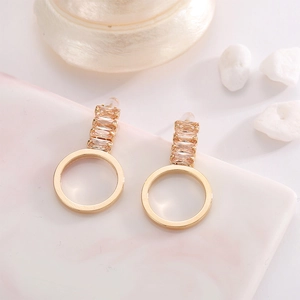 Détail de boucles d'oreilles dorées circulaires serties de zircons champagne taille baguette