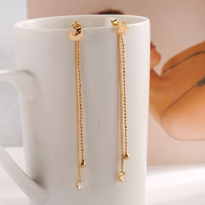 Detailed view of gold star and moon tassel earrings with zircon drops hanging on a cup
