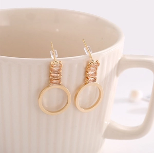 Boucles d'oreilles dorées avec zircone champagne suspendues sur une tasse en céramique