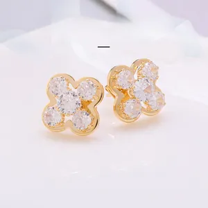 Vue macro des boucles d'oreilles trèfle dorées avec oxydes de zirconium sur ruban blanc