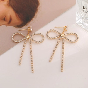 Détail de boucles d'oreilles papillon dorées avec pompons et incrustations de zircons